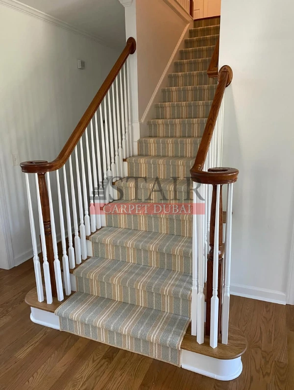 Completed project of Stair Carpet Dubai featuring a striped stair runner installation in neutral beige and grey tones on a wooden staircase with white railings.