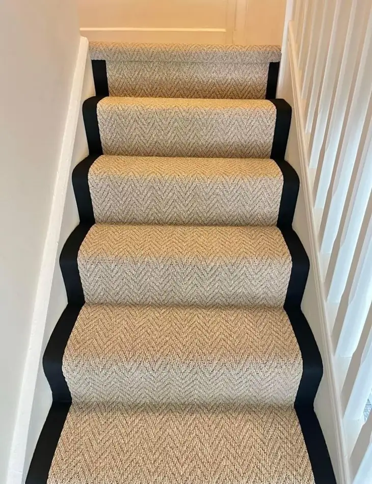 Beige herringbone stair carpet runner with black border installed on modern staircase