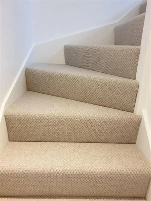 Close-up of winding stairs covered in a beige patterned Berber carpet with white trim.