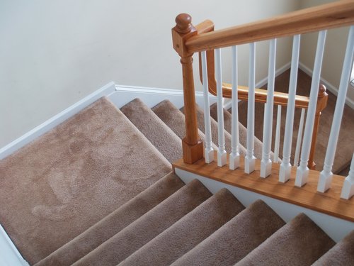 Wide wooden staircase covered in thick brown carpet with a classic handrail.