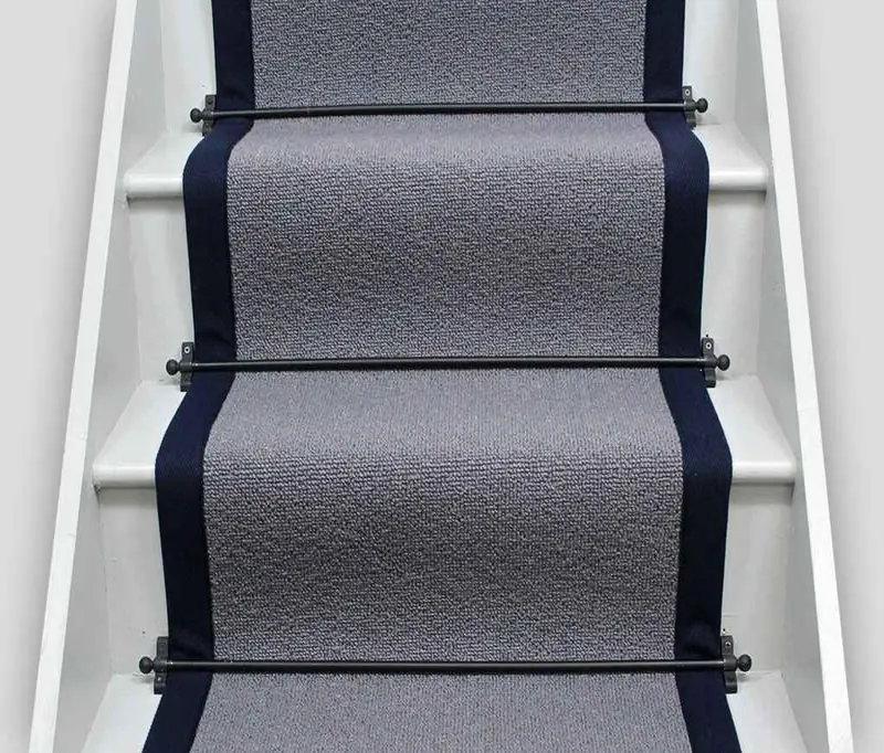 grey sisal stair runner with a solid navy blue fabric border installed on white stairs.