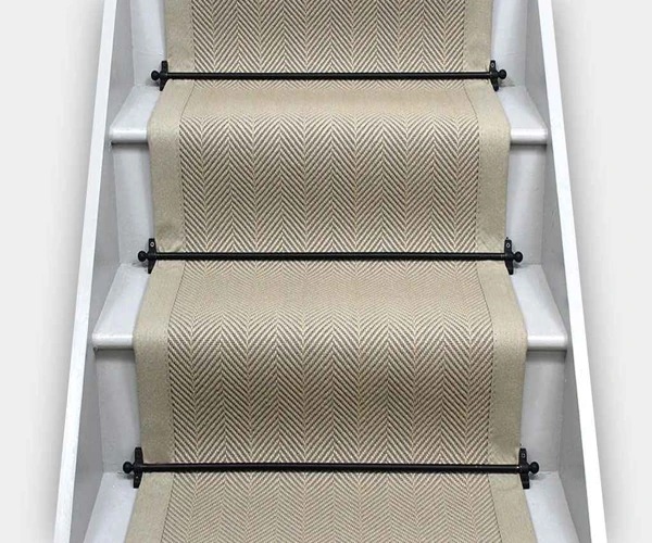 herringbone-patterned wool stair runner installed on white painted wooden stairs.
