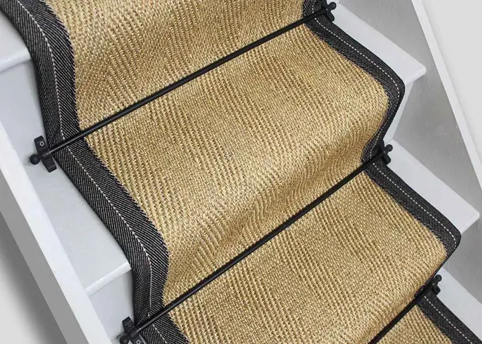 natural fiber stair runner with a black herringbone border and black metal stair rods on white painted stairs.