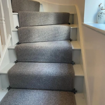 neutral grey woven stair runner with dark metal stair rods on white painted wooden stairs.