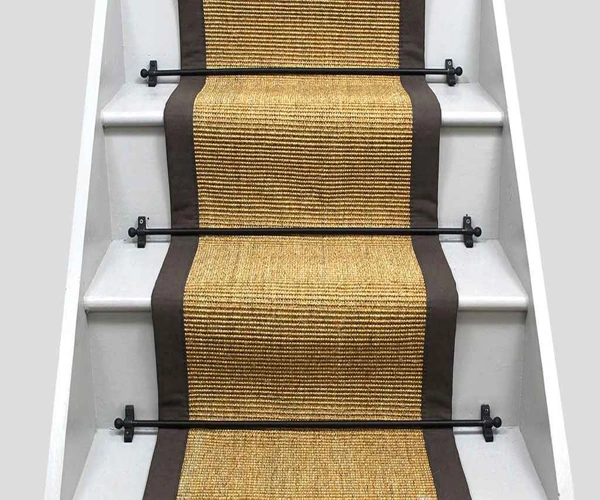 wooden staircase featuring a natural sisal carpet runner with a dark brown fabric border.