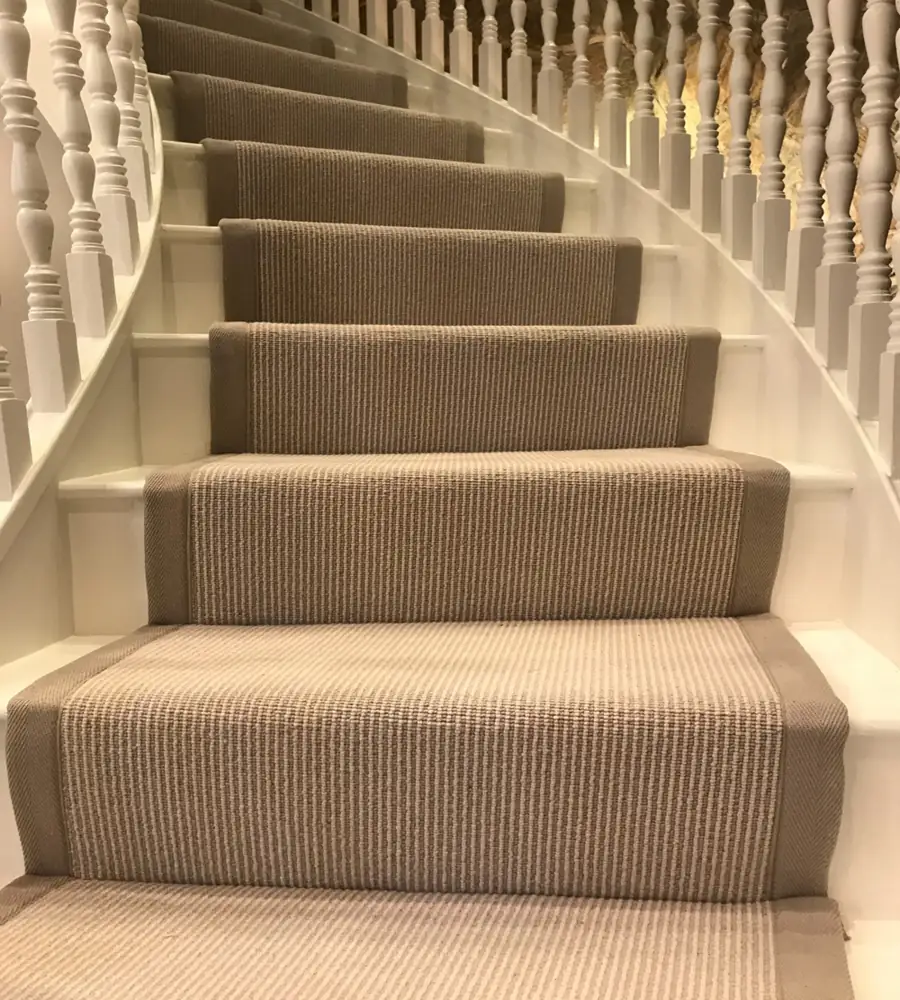 wooden staircase featuring a neutral-toned sisal carpet runner with beige fabric borders.