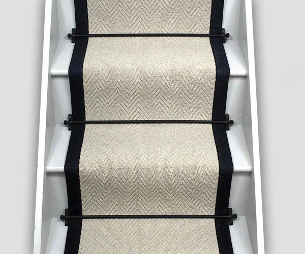 wool stair runner with black taped edges, secured to white stairs with black metal stair rods.