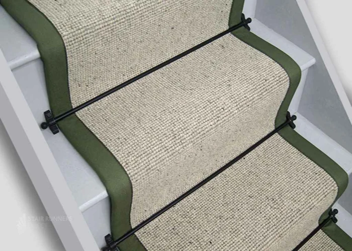 woven stair carpet runner with olive green fabric borders, secured to white wooden stairs by black metal stair rods.