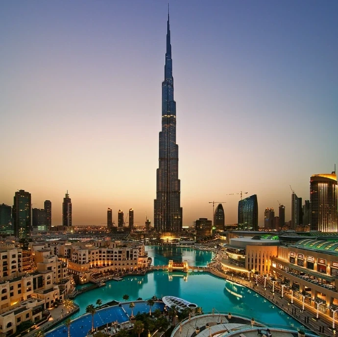 A sunset view of the Burj Khalifa towering over the Dubai skyline and the illuminated waterfront of Downtown Dubai.